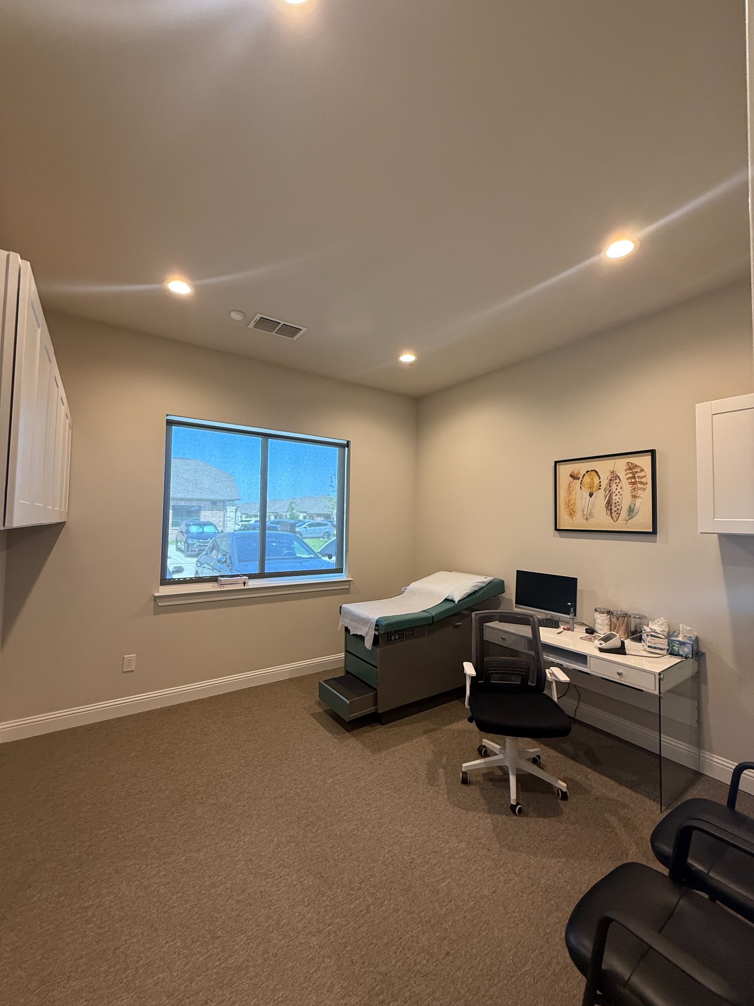 Clinic examination room with an exam table, desk, window, and patient seating